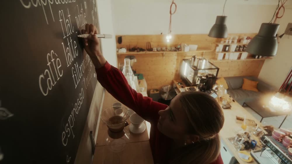 Baristka píše nabídku na tabuli v kavárně